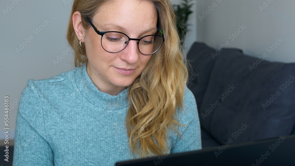 Young successful woman in glasses is actively working in office at the computer and enjoys her work. Female secretary is at her workplace typing on laptop. Woman tucking her blond hair behind her ear. Young successful woman in glasses is actively working in office at the computer and enjoys her work. Female secretary is at her workplace typing on laptop. Woman tucking her blond hair behind her ear.