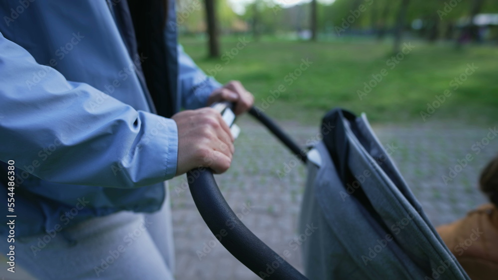 Closeup mother hands pushing baby carriage outside at park. Motherhood concept. Parent holding stroller handle Closeup mother hands pushing baby carriage outside at park. Motherhood concept. Parent holding stroller handle