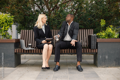 Black businessman sitting on a bench and talk with caucasian woman