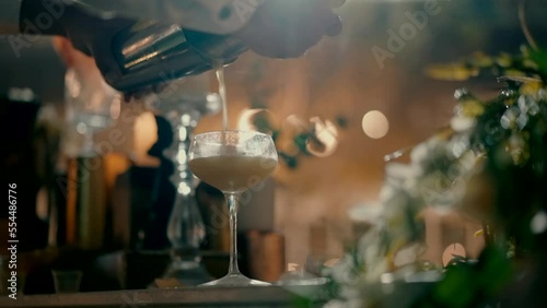 A bartender Shot from below of a bartender pouring a cocktail into a glass from a shaker at the bar. A bartender pours a cream-colored cocktail into a right glass from a shaker.