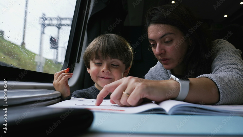 Mother helping child do his homework while traveling in high speed train. Parent teaching little boy with study activity while traveling in vacation