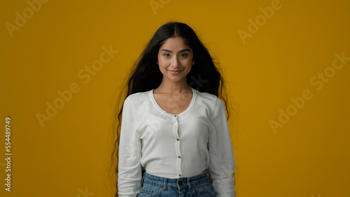 Ethnic Indian girl model with long hair gorgeous beautiful hairstyle in studio yellow background poising. Woman brunette with wavy shiny curls flying in wind hairdo silky hairstyling shampoo recovery