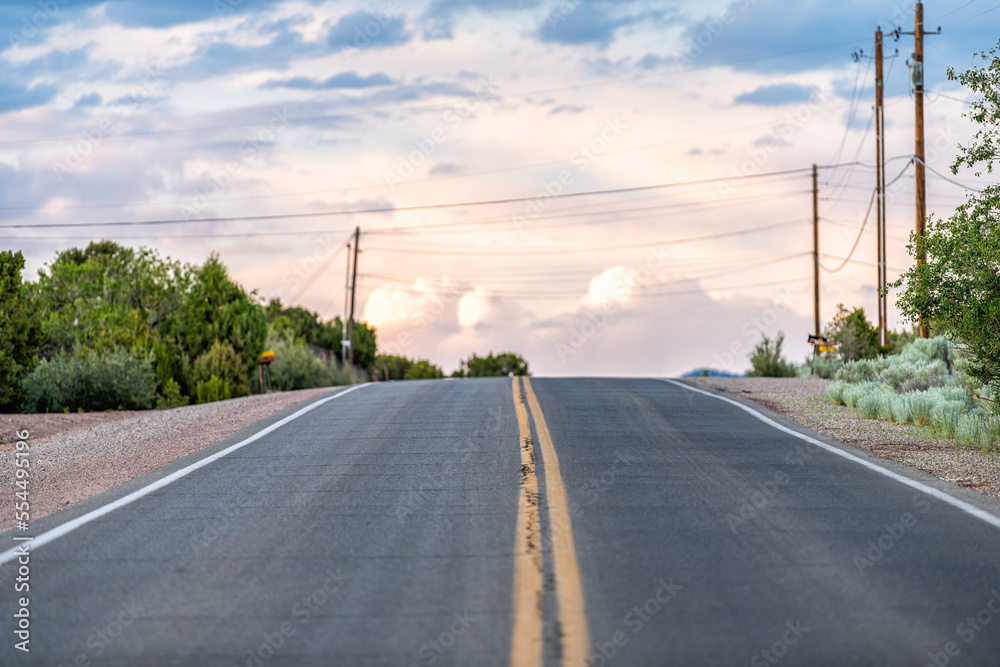 Colorful sunset on Bishops Lodge Road in Santa Fe, New Mexico with golden light, green plants and road to residential community