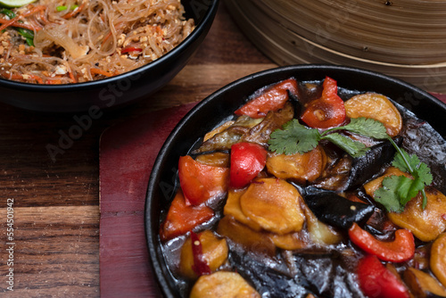 Delicious asian food in cast-iron pan on wooden background with wok with noodles. Selective focus. Asian food concept