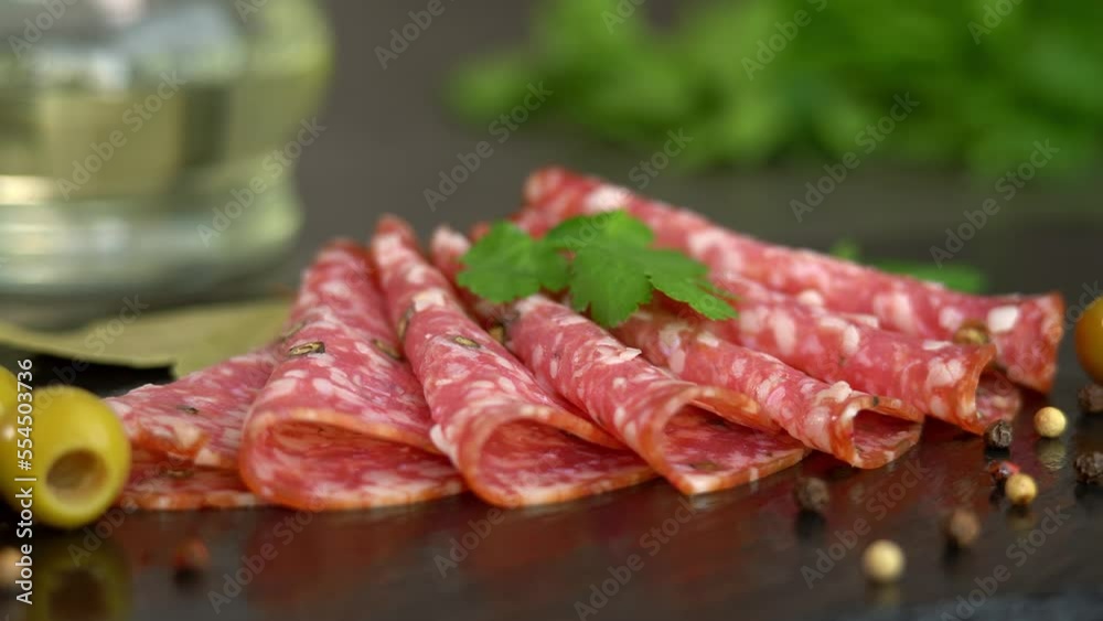 Camera movement on fresh slices smoked sausage with spices and seasonings on stone cutting board with olives and parsley. Cold cuts. Meat. Food Camera movement on fresh slices smoked sausage with spices and seasonings on stone cutting board with olives and parsley. Cold cuts. Meat. Food