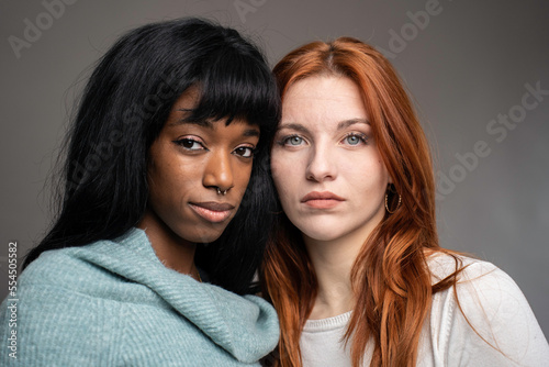 Couple of young women of different ethnicities - Red headed Caucasian woman with African female partner pose looking at camera - Multiculturalism and multiethnic concept - Focus on eyes