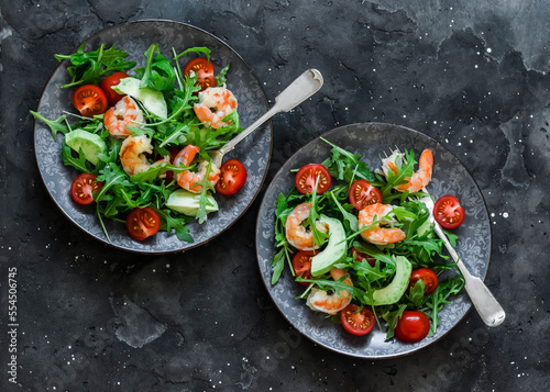 Shrimp, arugula,avocado, cherry tomatoes salad served on two plates on a dark background, top view