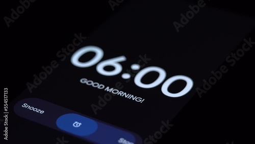 Good morning 6 am alarm clock on the phone, a finger taps stop. Close-up Focus on Mobile Phone Clock Showing Six A.M