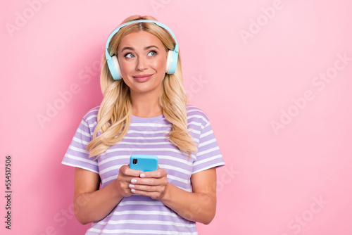 Photo of mature age blonde curly hair wear striped purple t-shirt dreaming hold phone listen music look empty space isolated on pink color background