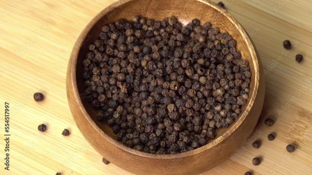 Peppercorns or black pepper spice lies in wooden bowl rotating. Dry seasoning in wooden bowl. Spices and herbs for cooking Peppercorns or black pepper spice lies in wooden bowl rotating. Dry seasoning in wooden bowl. Spices and herbs for cooking