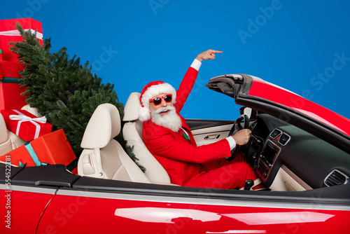 Photo of cool excited santa claus helpers wear costumes riding vehicle gifts delivery pointing empty space isolated white color background © deagreez