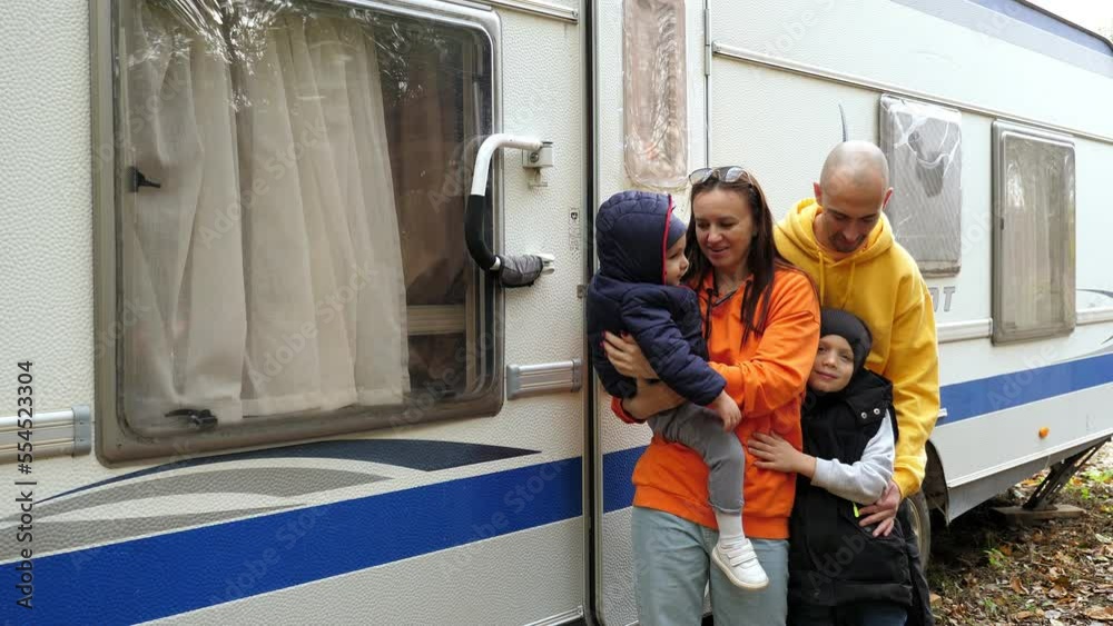 A happy family with little children on a hike is resting in the autumn forest in a motorhome. Trailer for camping.