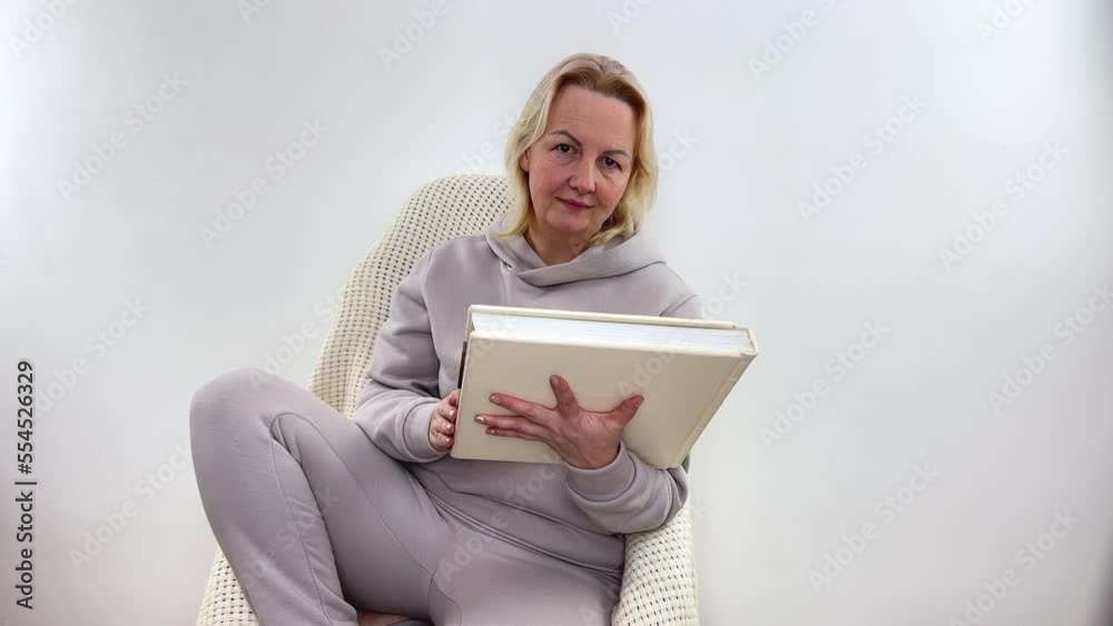 Woman hugging album dreaming remembering something in light-colored tracksuit holds album with white beige pages in hands opens empty space for advertising holding book in front of gray background Woman hugging album dreaming remembering something in light-colored tracksuit holds album with white beige pages in hands opens empty space for advertising holding book in front of gray background