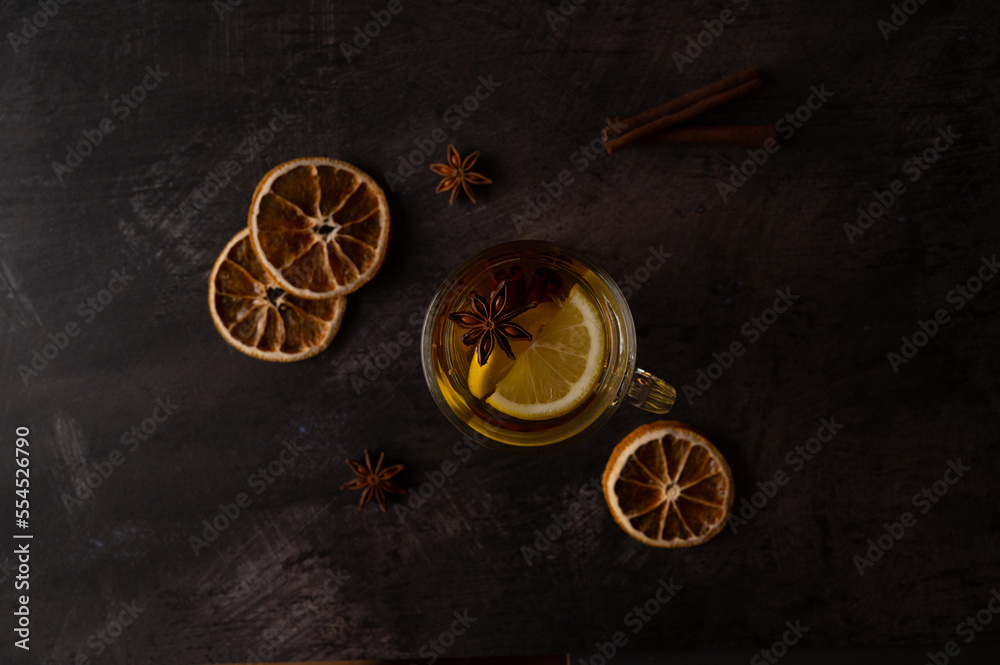 Black tea with lemon slices, star anise and cinnamon in a glass teacup on a black metallic background. Top view.