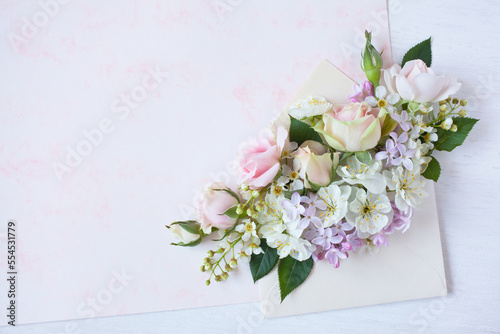 Bouquet of pink roses, lilacs, bird cherry, white fruit flowers in an envelope on white-pink decorative paper. Holiday greeting card, copy space