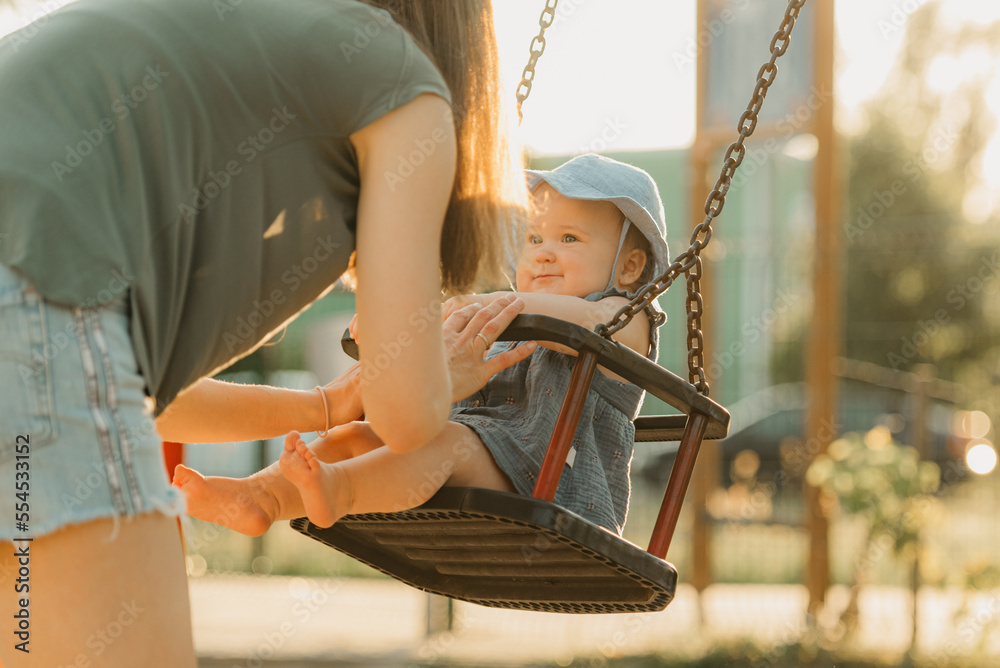 Baby girl in a dress with her mother on a swing on the warm summer evening