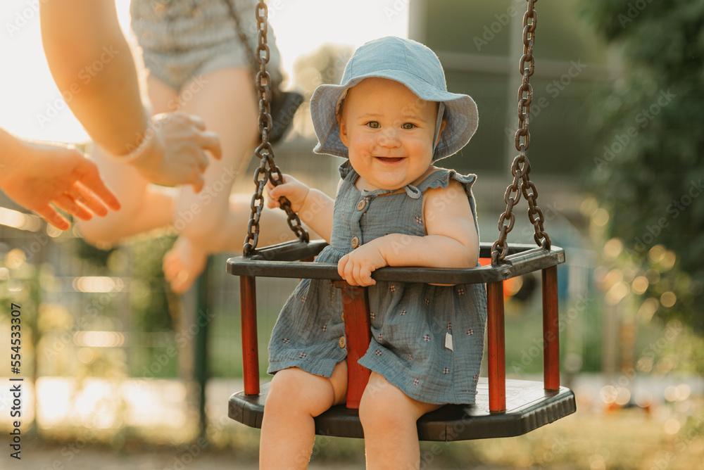 Toddler with her mom in a dress is joying on a swing on the warm summer evening