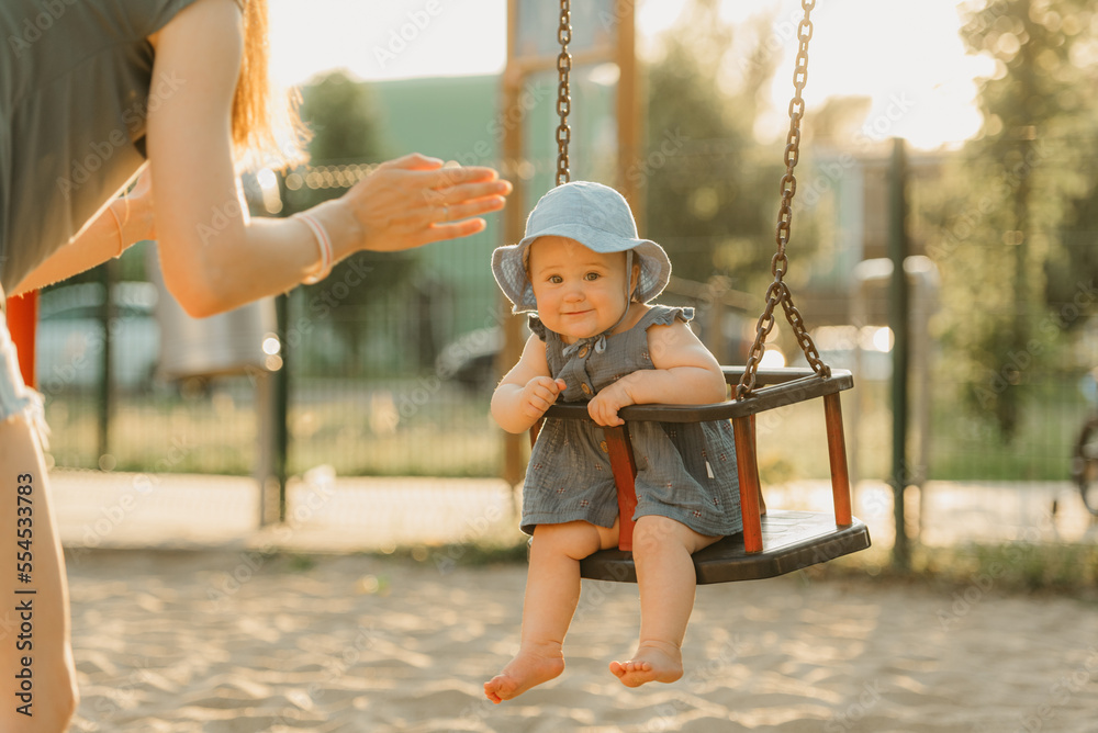 Toddler baby girl is enjoying on a swing on the warm summer evening