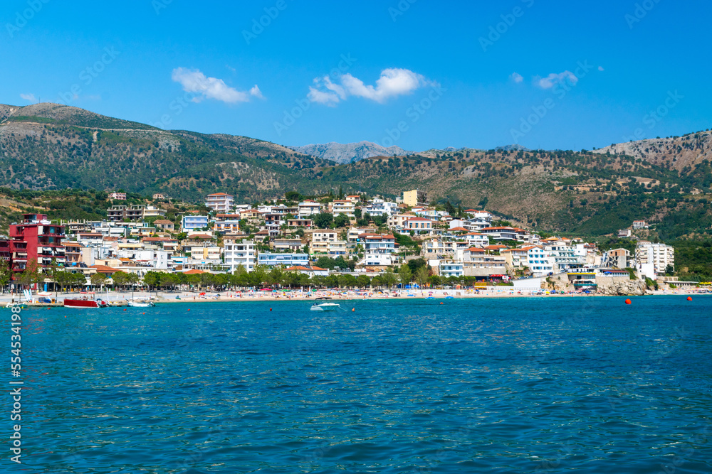 Fototapeta premium Beautiful summer cloud landscape of beach town of Himare at foot of mountains on border of Ionian and Adriatic seas. Albania