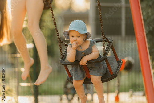Obraz na płótnie Toddler in a dress is sucking her thumb on a swing on the warm summer evening w salonie