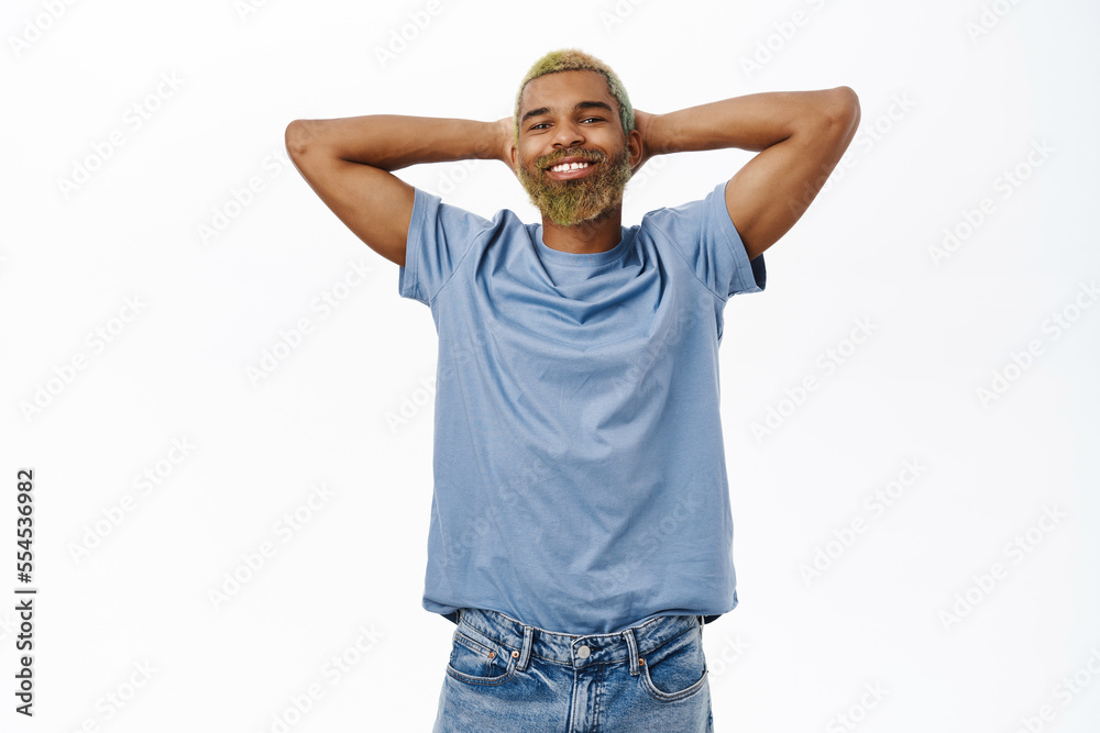 Portrait of handsome happy young man without worries, holds hands behind head and rests, laying lazy and smiling pleased, standing over white background Portrait of handsome happy young man without worries, holds hands behind head and rests, laying lazy and smiling pleased, standing over white background