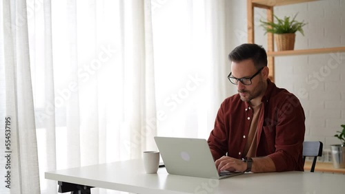 Hard work makes the vision happen. Young satisfied businessman using a laptop sitting at the desk at home. Home office. Working from home. He feels satisfied and proud of his work.