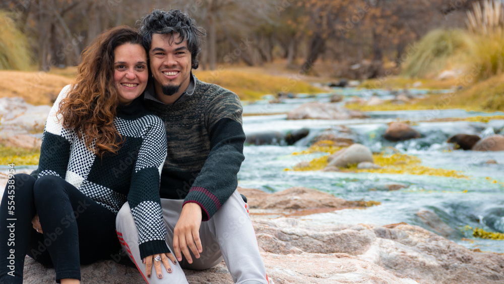 Nice couple sitting smiling in a park near the river in winter Nice couple sitting smiling in a park near the river in winter