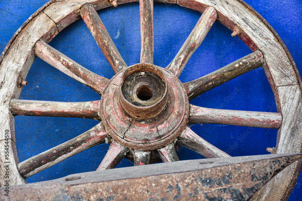 Wooden wheel of an old wagon on a blue washed wall and antique wrought iron tool in front	