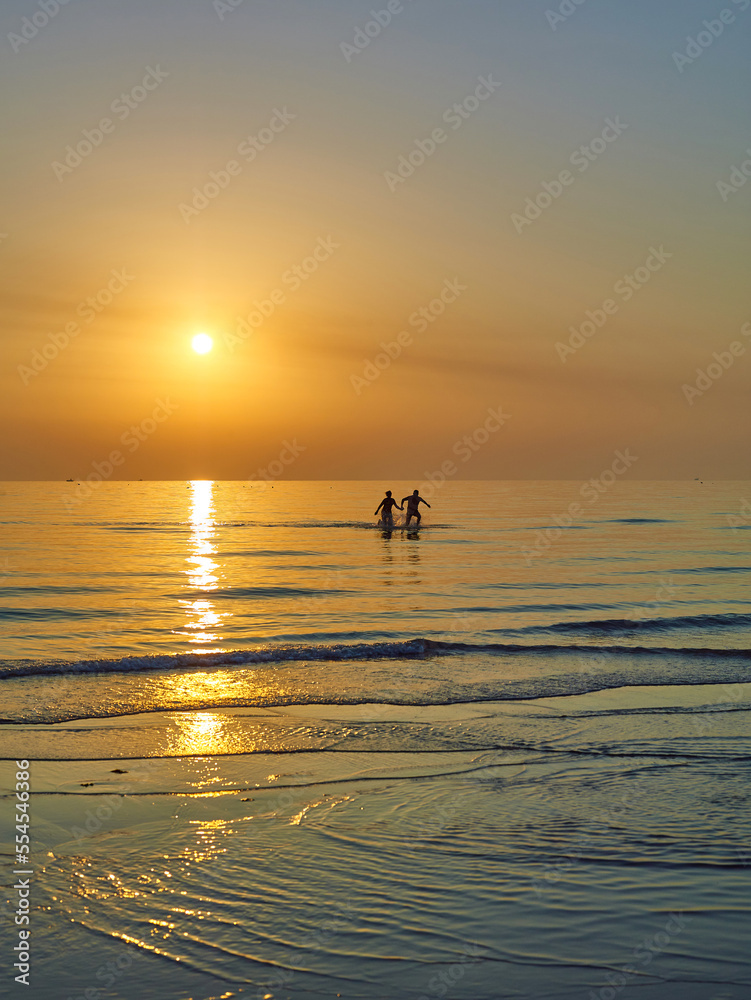 Couple are walking along the sunset beach