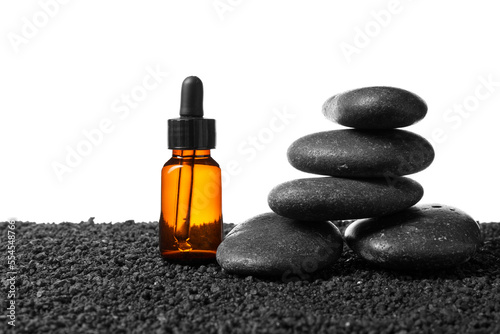 Cosmetic dropper bottle with spa stones on sand against white background