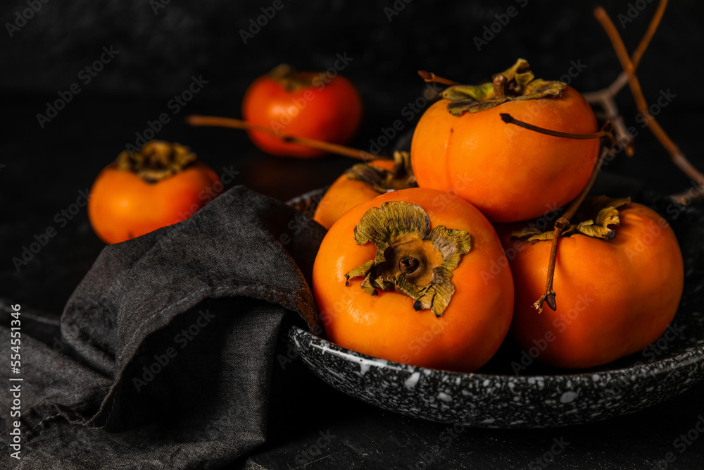 Bowl of ripe persimmons on dark background, closeup