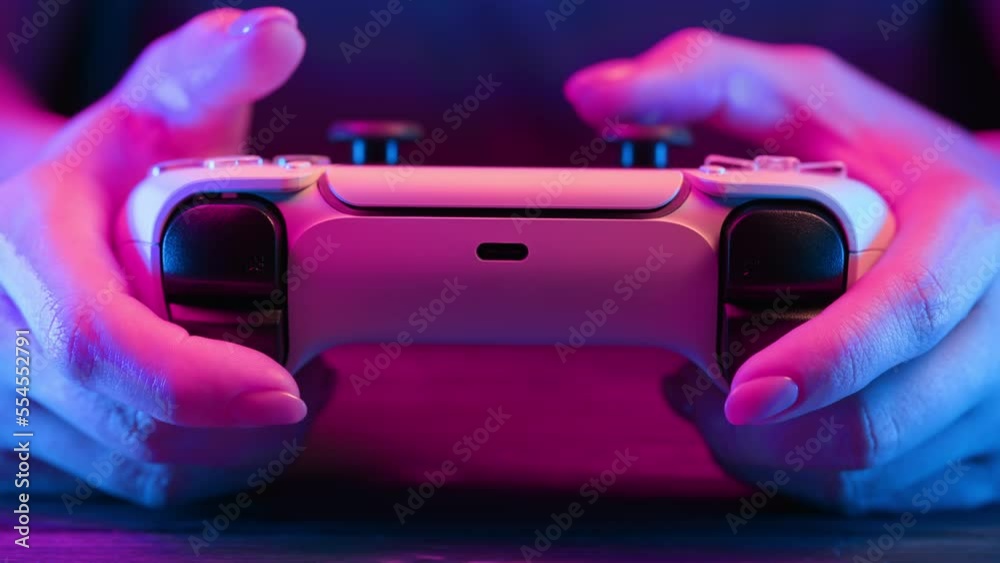 Gamer's hands playing online video game on console TV with joystick, neon color light. Woman presses buttons, using joypad controller, newest wireless gamepad. Hobby, e-sport, macro view