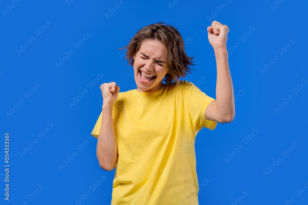 Pretty woman shows triumph yes gesture of victory, she achieved result, goals. Girl glad, happy, surprised excited happy lady on blue background. Jackpot concept.