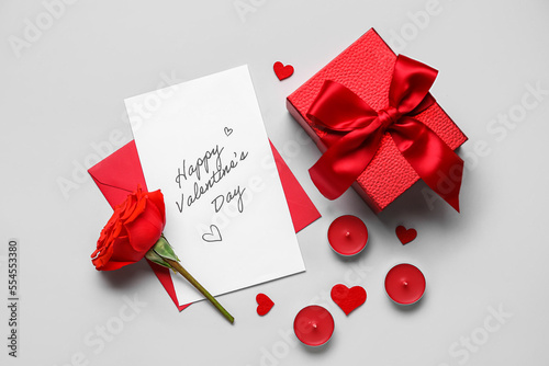 Letter with text HAPPY VALENTINE'S DAY, rose, candles and gift on grey background