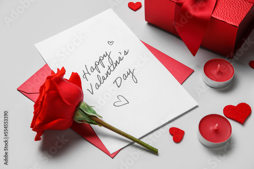 Letter with text HAPPY VALENTINE'S DAY, rose, candles and gift on grey background