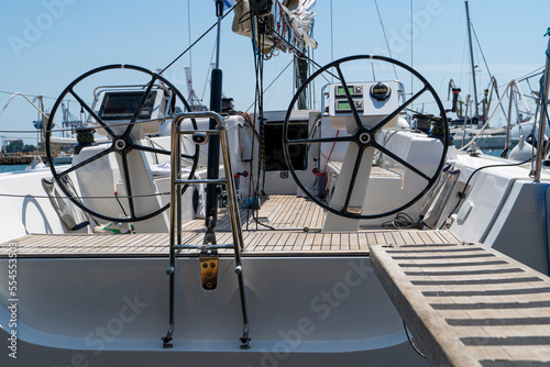 White sailing yacht on the quay in the port on a cloudy day, view from the stern. High-quality photo. boat stern with big steering wheel and sailboat stern deck. Close-up © Alexey Lesik