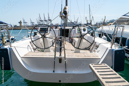 White sailing yacht on the quay in the port on a cloudy day, view from the stern. High-quality photo. boat stern with big steering wheel and sailboat stern deck. Close-up