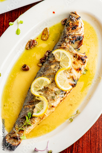 Grilled Fish. Branzino, whole grilled sea bream. Classic regional Greek  seafood favorite. Whole fish, grilled with skin in, served with lemon potatoes lemons Italian parsley and capers.