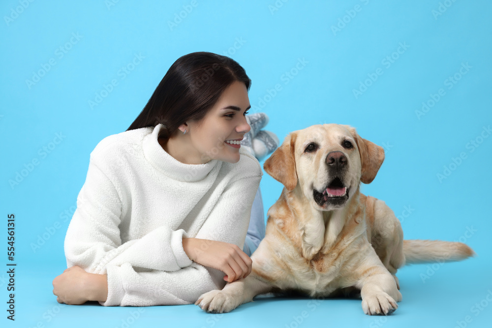 Happy woman with cute Labrador Retriever on light blue background