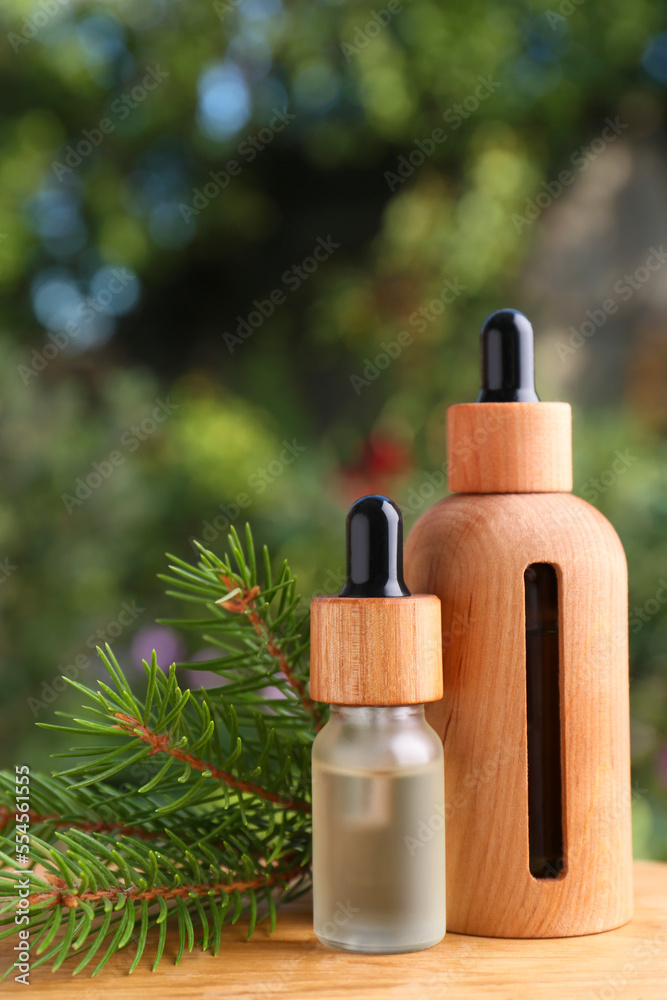 Bottles of pine essential oil and branches on wooden table against blurred background, closeup Bottles of pine essential oil and branches on wooden table against blurred background, closeup