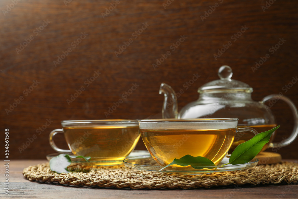 Fototapeta premium Fresh green tea in glass cups, leaves and teapot on wooden table
