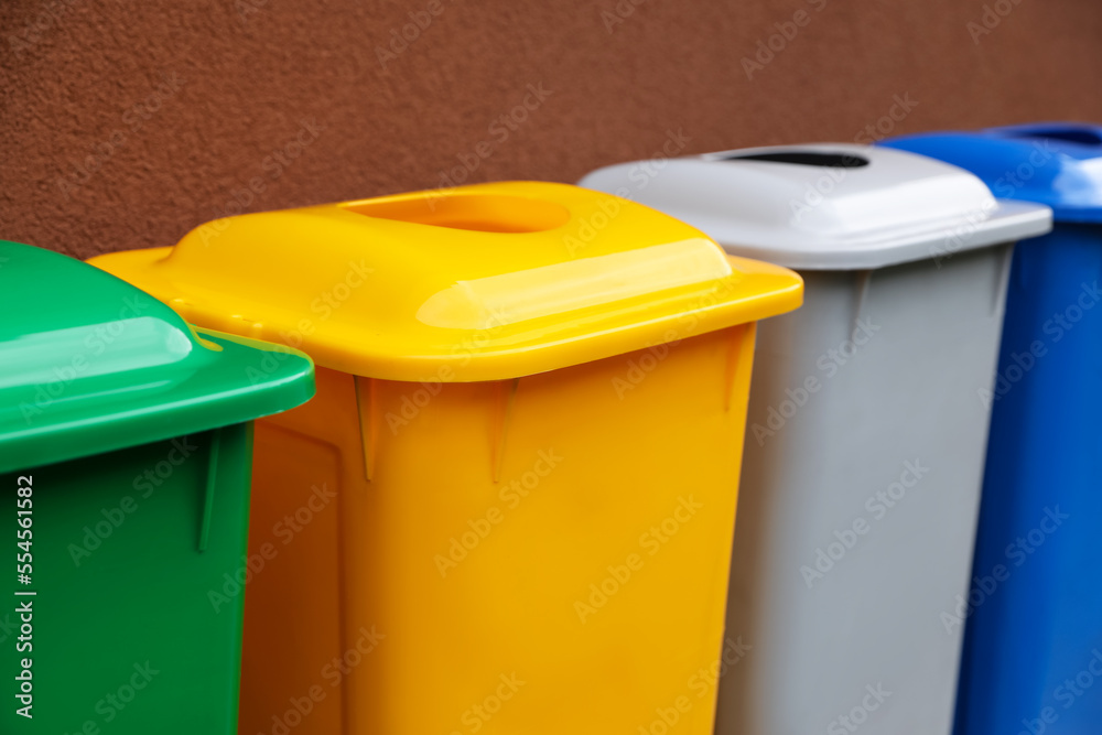 Many color recycling bins near brown wall, closeup Many color recycling bins near brown wall, closeup