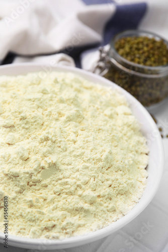 Mung bean flour in bowl and seeds on white tiled table, closeup