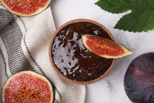 Bowl of tasty sweet fig jam and fruits on white marble table, flat lay