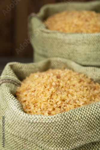 Burlap bags with uncooked bulgur on wooden background, closeup