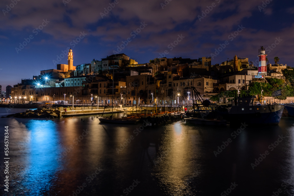 Panorama of an ancient port and a city with ships, boats, a light tower and a church, blue sky and gray clouds, with a long exposure on the water