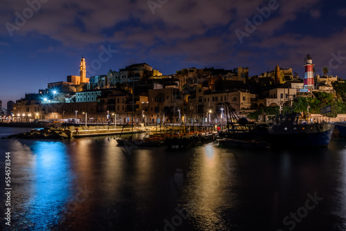 Panorama of an ancient port and a city with ships, boats, a light tower and a church, blue sky and gray clouds, with a long exposure on the water