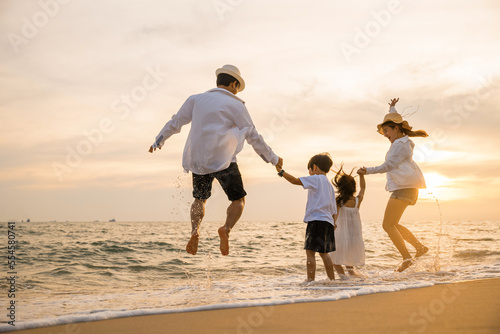 Happy Asian family have fun jumping together on beach in holiday at sunset time, Silhouette of family holding hands live healthy lifestyle on beach, back people enjoying travel and vacations concept