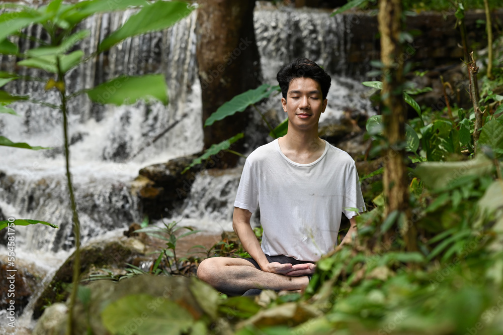 Millennial Young Asian man doing meditation as the waterfall on the background. Millennial Young Asian man doing meditation as the waterfall on the background.