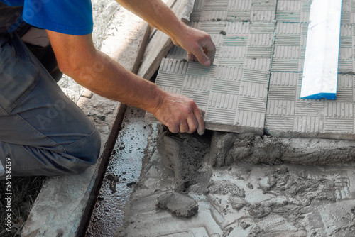 Bricklayer lays tiles on cement. Photo of hand with tile close-up. Authentic workflow. Construction background..